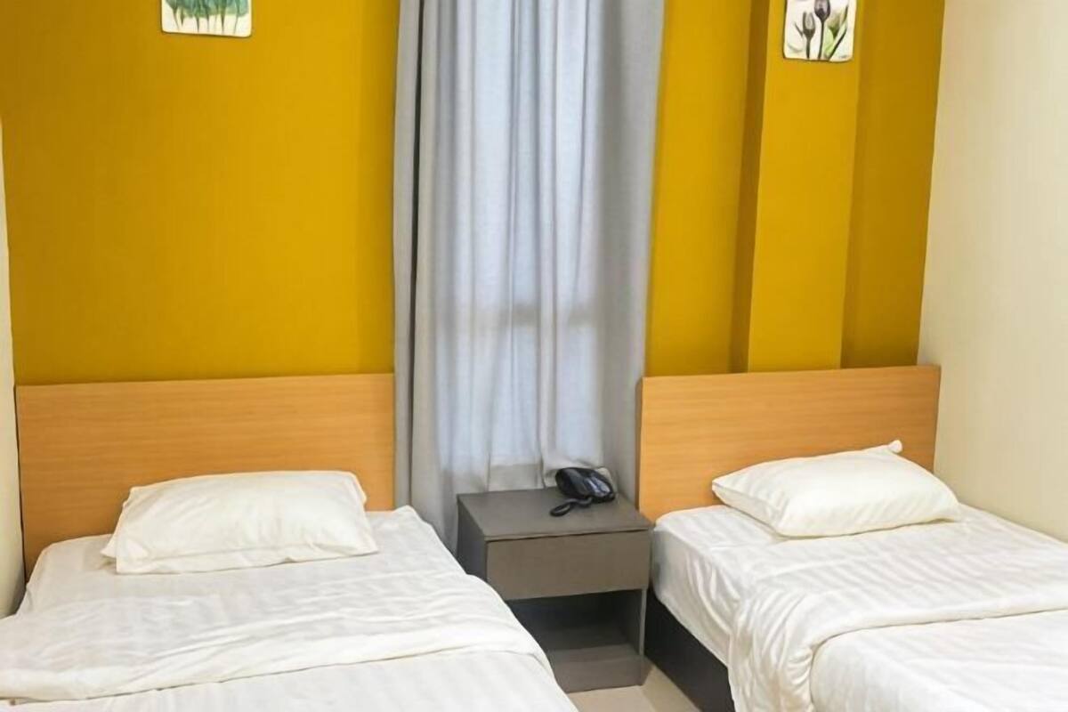 A hotel room with two beds, a nightstand with a phone, and a curtain.