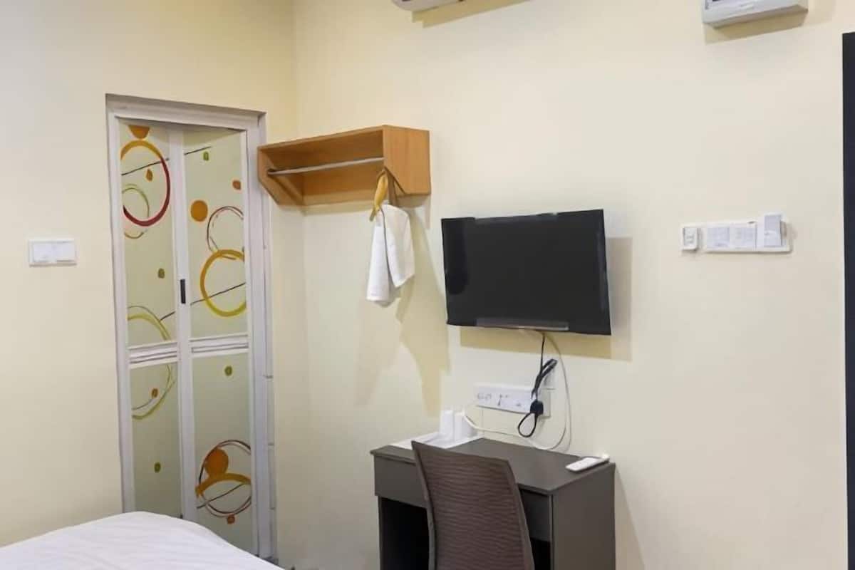 A hotel room with a bed, a desk with a chair, a television mounted on the wall, and a wardrobe with a decorative door.