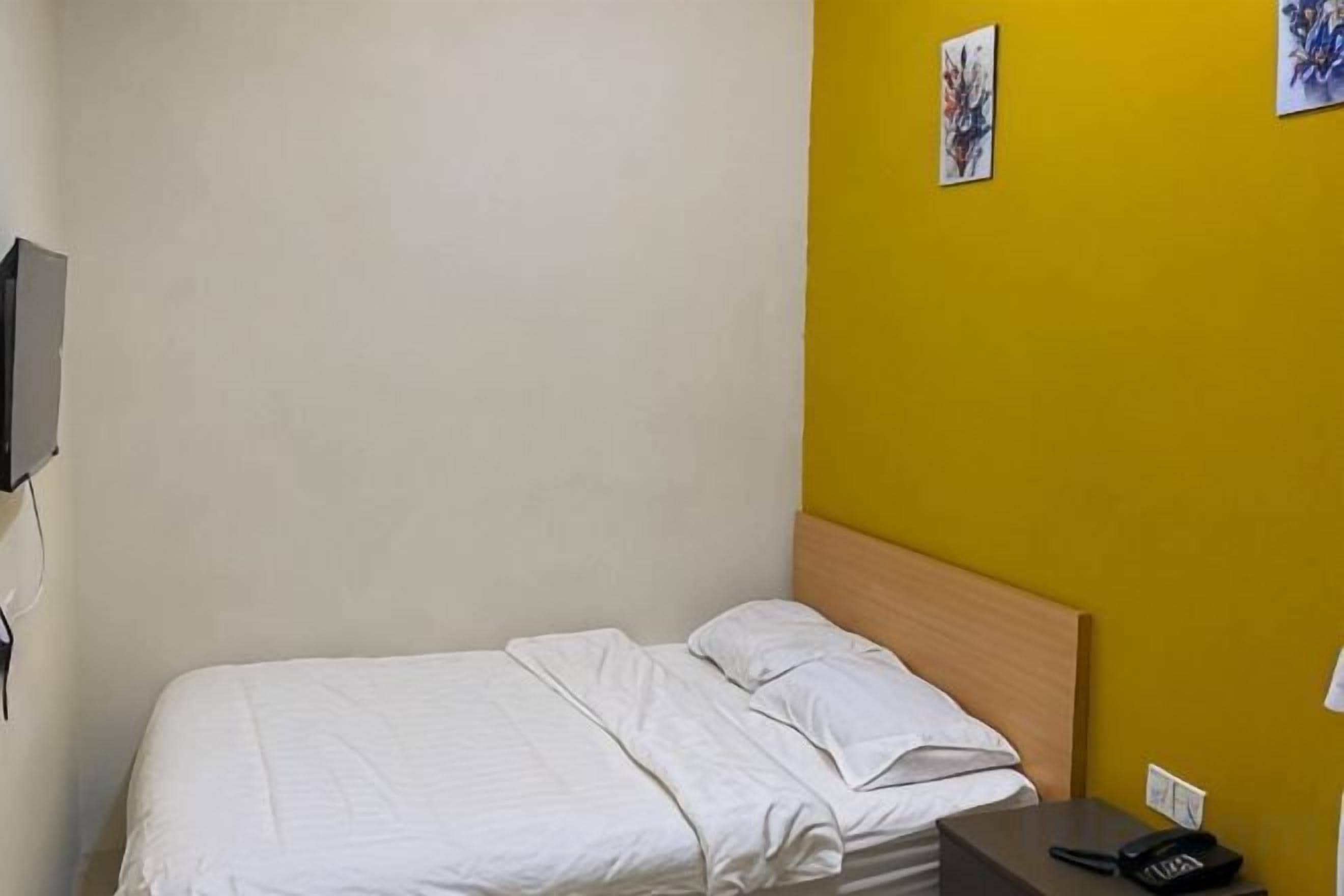 A single bed with a wooden headboard in a room with a yellow wall.
