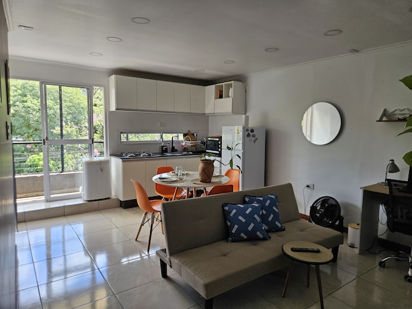 A modern kitchen with white cabinets, a dining table with orange chairs, and a sofa with blue pillows.