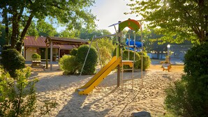 A playground with a yellow slide, a climbing structure, and a sand area.