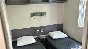 A compact bedroom with two single beds, a small bedside table, and a shelf above the beds.
