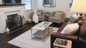 Uma sala de estar com lareira, televisão, sofá, mesa de centro e abajur.