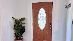 Uma porta de madeira com painel de vidro e design decorativo, um vaso com planta e uma luminária fixada na parede.