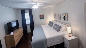 Quarto com uma cama, televisão, ventoinha no teto e obras de arte na parede.
