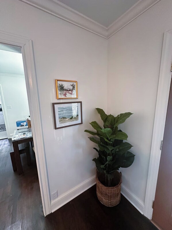 A corner of a room with white walls, two framed pictures, and a large green plant in a wicker basket. - Just updated! Downtown Greer house. Walk to downtown shops. Fenced in backyard (Greer)