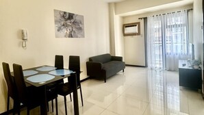 A modern living room with a dining area, a gray sofa, and a large window with curtains.