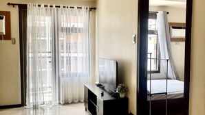 A modern hotel room with a large mirror, a flat-screen TV on a black stand, a small plant, and a bed with a canopy.