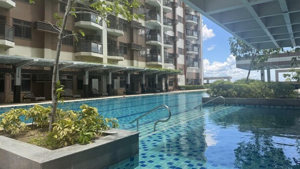 A swimming pool with a tiled floor, surrounded by a building with balconies and a covered area.