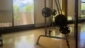 A gym with a weightlifting station, large windows, and a view of greenery outside.