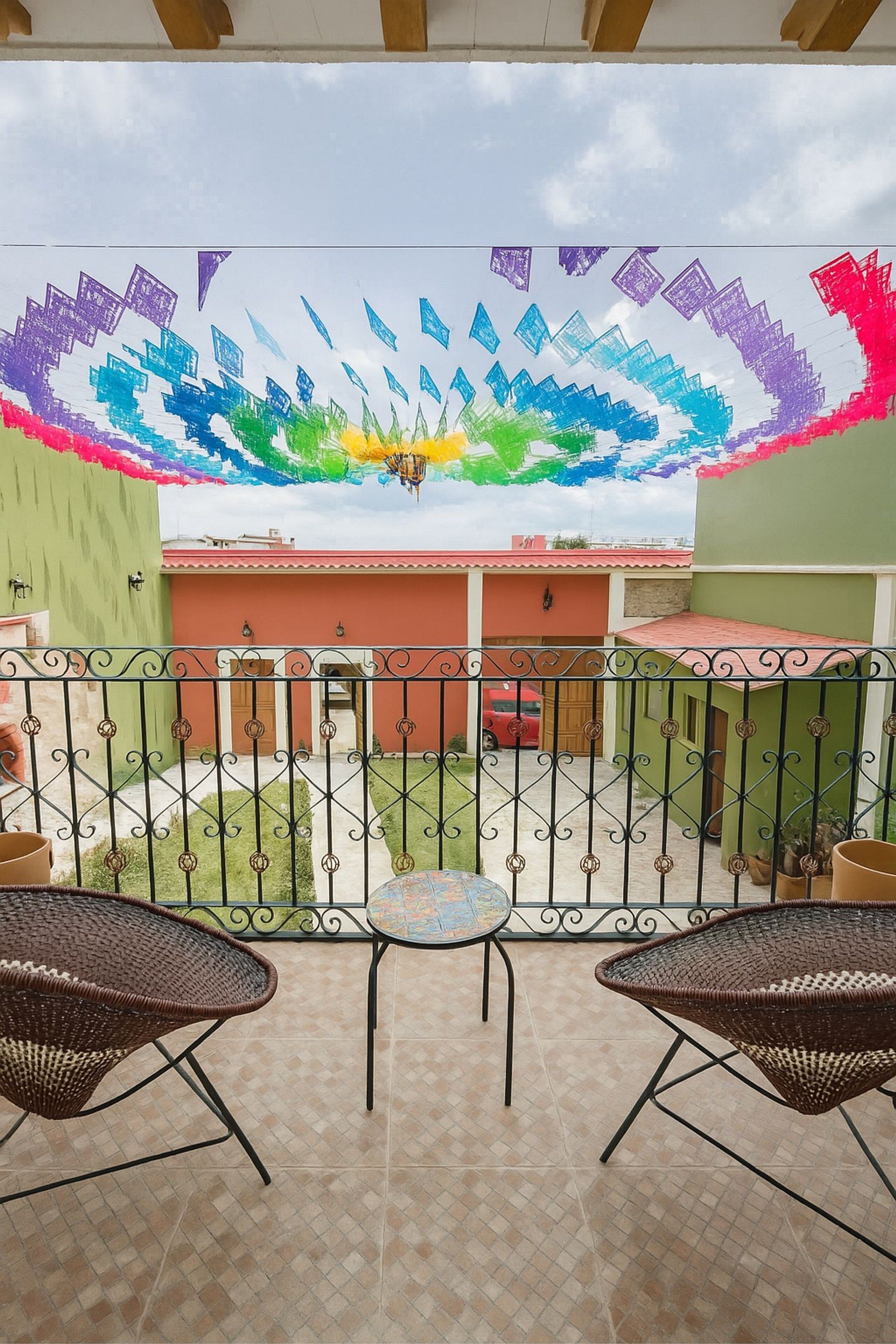 A balcony with a view of a courtyard, featuring a decorative wall and a red car parked in the background.