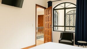 Camera d'albergo con un letto grande, una televisione montata a parete, una sedia e una finestra con tende.