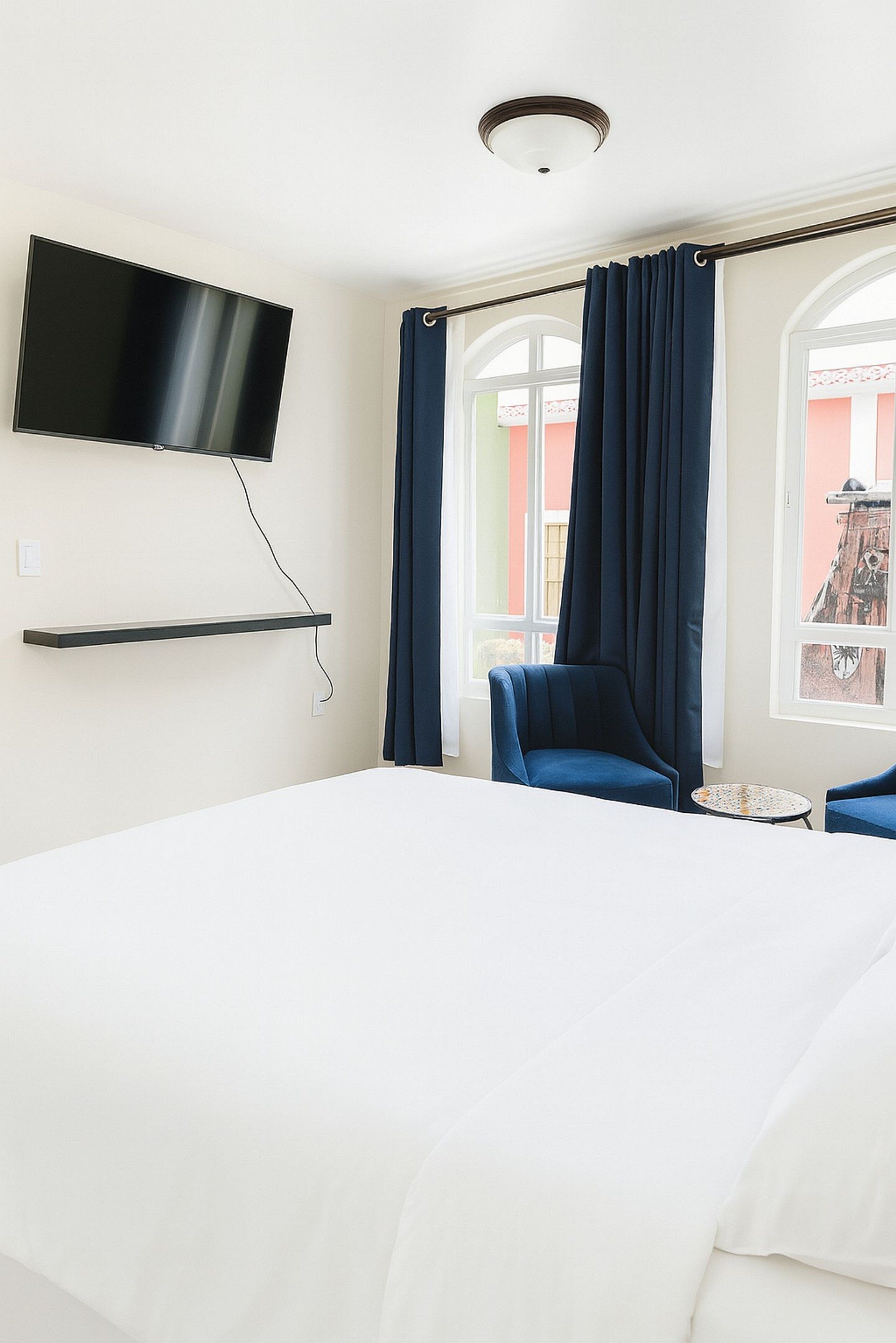 A hotel room with a bed, a TV mounted on the wall, a chair, and a small table.
