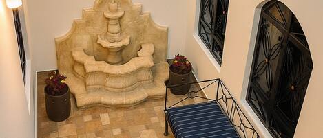 Una habitación pequeña y acogedora con una fuente de piedra, un banco y plantas en macetas.