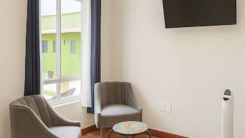Una camera d'albergo con un letto, due poltrone, un tavolino, una televisione e una finestra con tende.