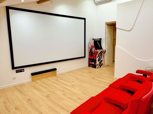 A modern room with a large screen, a gaming console, and red seating. - CINEMA Lune (Montfrin)