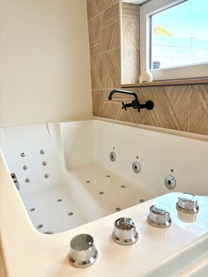A modern bathroom with a freestanding bathtub, a window above it, and a herringbone-patterned wall. - CINEMA Lune (Montfrin)