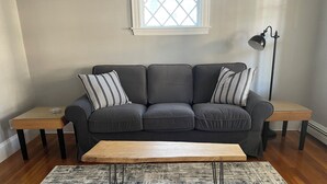 Un salon avec un canapé gris, deux coussins à rayures, une table basse en bois, un tapis à motifs et un lampadaire.