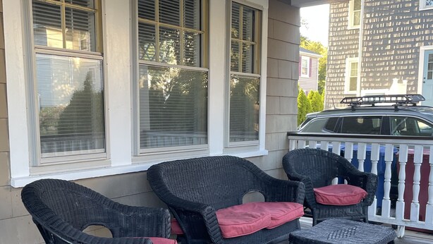 Une véranda couverte, meublée de meubles en osier, avec une voiture garée au fond.