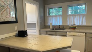 Une cuisine avec un îlot central recouvert de carreaux, un lave-vaisselle, un évier et une fenêtre avec des rideaux.