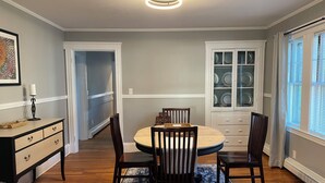 Un coin repas comprenant une table ronde, quatre chaises, un tapis à motifs bleus, un meuble avec des portes en verre et un luminaire au plafond.