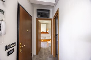 A hotel hallway with a wooden door, a phone, and a bed in the adjacent room.