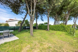 A backyard with a barbecue grill, a table with chairs, and a hedge.