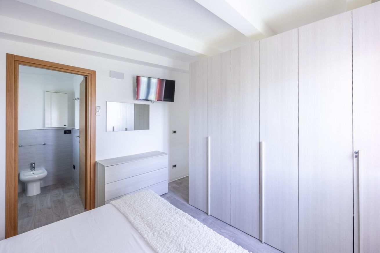 A bedroom with a bed, a wardrobe, a TV, a mirror, and a bathroom visible through an open door.