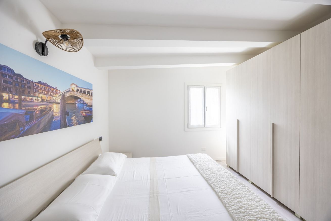 Une chambre à coucher avec un lit, un tableau représentant un pont, une fenêtre et une armoire.