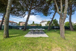 An outdoor seating area with a table and chairs, surrounded by trees and a grassy lawn.