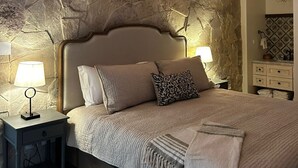 Ein Schlafzimmer mit Steinsandsteinwand, einem Bett mit Kopfteil, zwei Nachttischen mit Lampen und einem Beistelltisch.