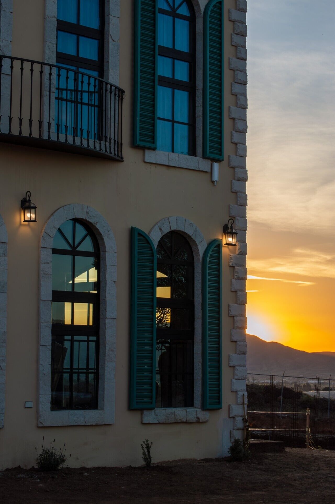 Un bâtiment doté de nombreuses fenêtres en arc de cercle et de volets verts, avec un balcon orné d’une rambarde en métal.