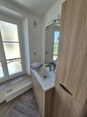 Ein modernes Badezimmer mit großem Fenster, Waschbecken mit Spiegel und Holzschränken.