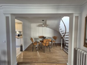 Een eetruimte met een glazen tafel, houten stoelen, een plafondventilator en een spiltrap.