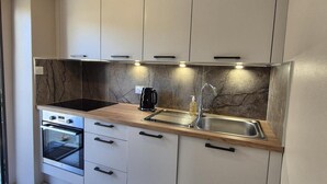A modern kitchen with white cabinets, a marble backsplash, a built-in oven, a coffee maker, and a stainless steel sink.
