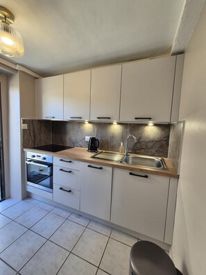 A modern kitchen with white cabinets, a marble backsplash, a built-in oven, a coffee maker, and a stainless steel sink. - Bleautiful Diane : private apartment (Fontainebleau)