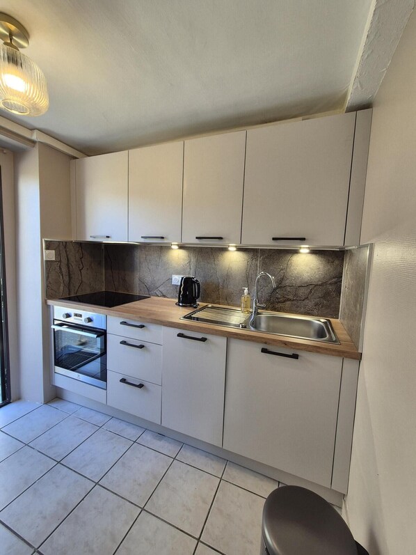 A modern kitchen with white cabinets, a marble backsplash, a built-in oven, a coffee maker, and a stainless steel sink.