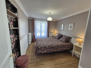 Ein Schlafzimmer mit Bett, Nachttisch, Lampe, Heizkörper und einem Fenster mit Vorhängen.