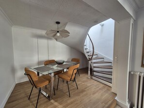 A dining area with a glass table, four chairs, a ceiling fan, and a spiral staircase.