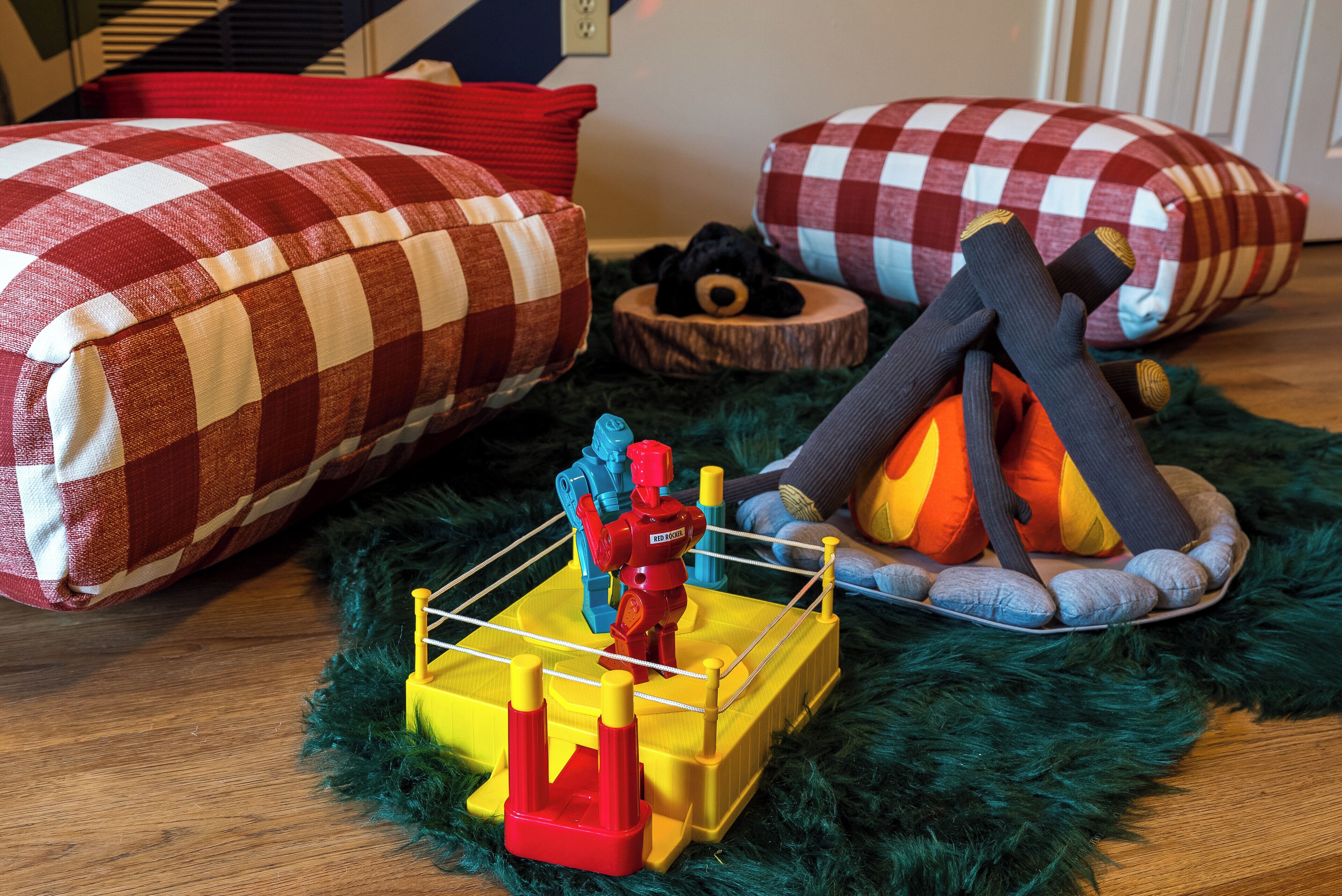 A room with a checkered bedspread, a small wooden bed, a toy boxing ring, and a plush toy.