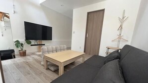 A living room with a sofa, a table, a TV, a plant, and a door. - Minami Otaru House Sakaimachi (Otaru)