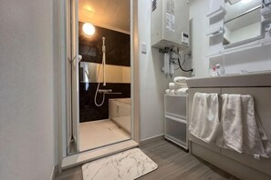Een moderne badkamer met een douchecabine van glas, een marmeren vloer en een wit badkamer meubel met handdoeken.