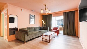 Un salon avec un canapé, une table basse et un fauteuil. Il y a une fenêtre avec des rideaux, une porte et un luminaire fixé au mur.