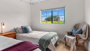 A bedroom with a bed, a chair, a nightstand, and a window with a view of greenery.