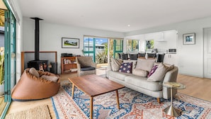 A modern living room with a sofa, coffee table, and a fireplace. There is a dining area with a table and chairs.
