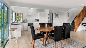 A modern kitchen with white cabinets, a dining table with black chairs, and a staircase.