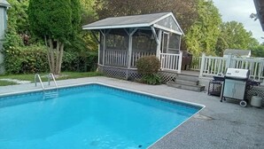 Ein Schwimmbecken mit überdachter Liegefläche, Grill und einer kleinen Gartenhütte.
