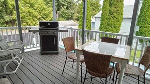 Eine überdachte Terrasse im Freien mit Grill, Korbstühlen und einem Tisch.