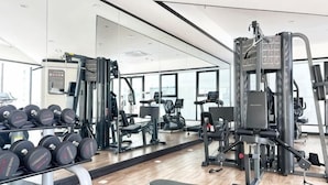 A gym with weightlifting equipment, a bench, and a mirror reflecting the space.