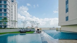 A swimming pool with a wooden deck, surrounded by buildings and trees.